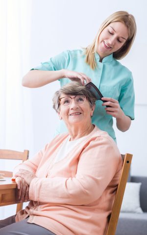 Young female caregiver doing senior woman's hair